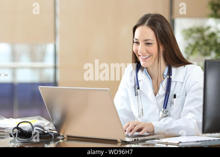 Happy doctor using a laptop writing content at consultation Stock Photo