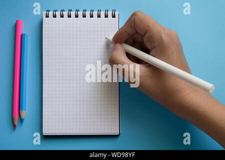 Woman hand writing in blank notebook on a two color background. Trendy pink and blue colors. Back to school concept. Mock up, flat lay. Stock Photo