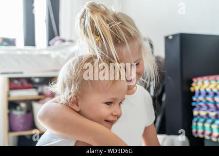 Cute adorable blond caucaian little sister hugging her toddler brother.couple of cheerful sibling playing indoor. Cute girl and baby boy enjoy