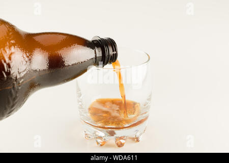 dark drink from a large bottle poured into a transparent glass Stock Photo