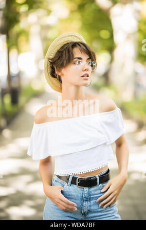 Young woman wearing straw hat showing her teeth while walking in green park Stock Photo