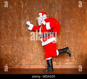 Santa Claus walking with the big red bag of the presents on the brown background Stock Photo