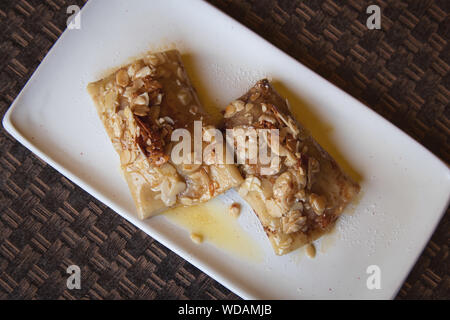 Russian pancakes with cottage cheese filling and sliced almonds and honey on the top. Delicious dessert on the white plate. Stock Photo