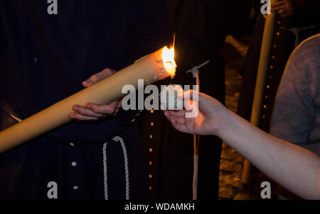 Closeup of the hand of a kid collecting wax for his wax-ball during the Holy Week in Seville, Andalusia, Spain. Nocturnal procession. Stock Photo