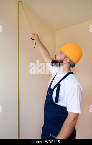 Construction worker and handyman is working on renovation of apartment. Builder is measuring wall of room using measure tape at construction site. Stock Photo
