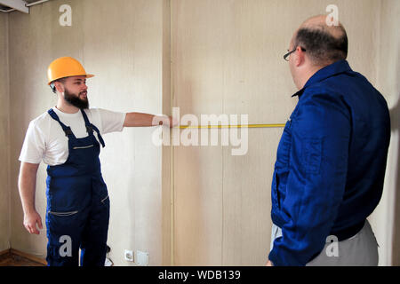 Engineer, contractor and project manager with his colleague, construction worker, handyman and builder is measuring wall using measure tape. Stock Photo
