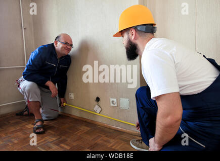 Engineer, contractor and project manager with his colleague, construction worker, handyman and builder is measuring wall using measure tape. Stock Photo