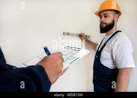 Engineer, contractor and project manager with his colleague, construction worker, handyman and builder is measuring wall using spirit level tool. Stock Photo
