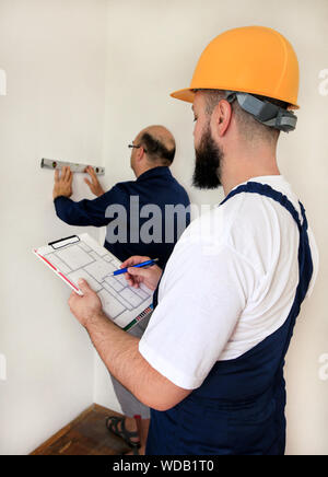 Engineer, contractor and project manager with his colleague, construction worker, handyman and builder is measuring wall using spirit level tool. Stock Photo