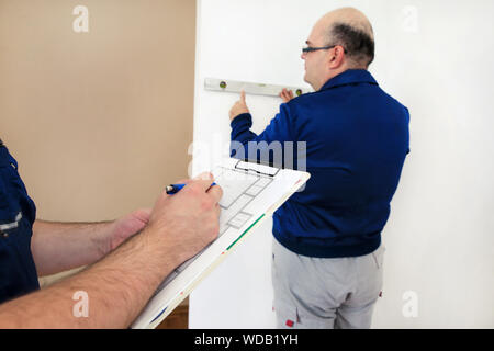 Engineer, contractor and project manager with his colleague, construction worker, handyman and builder is measuring wall using spirit level tool. Stock Photo