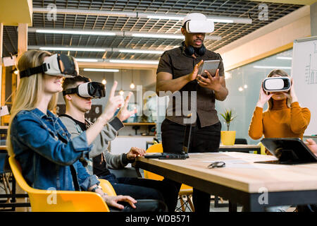 Group of positive colleagues testing virtual reality glasses. Handsome African businessman developing a project using virtual reality goggles Stock Photo