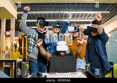 Expressive young multiethnical people wearing virtual reality goggles watching movies or playing video games. Cheerful African man with VR glasses sit Stock Photo