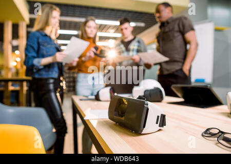 Blurred image of five multiethnical business persons are developing a project using modern gadgets and virtual reality goggles. Focus on the VR goggle Stock Photo