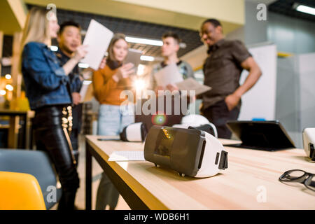 Blurred image of five multiethnical business persons are developing a project using modern gadgets and virtual reality goggles. Focus on the VR goggle Stock Photo