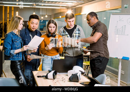 Multiracial business team using tablet, laptop and virtual reality headsets in office meeting. Developers meeting with virtual reality simulator aroun Stock Photo