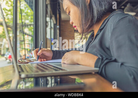 Asian millennial working on laptop and writing notes Stock Photo