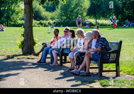Friends sit together on benches in a park at Marlow, Buckinghamshire, UK Stock Photo