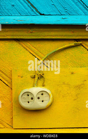 Old-fashioned electrical outlet with a cut-off wire on a yellow-blue wooden wall closeup Stock Photo