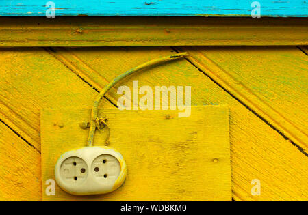 Old-fashioned electrical outlet with a cut-off wire on a yellow-blue wooden wall closeup Stock Photo