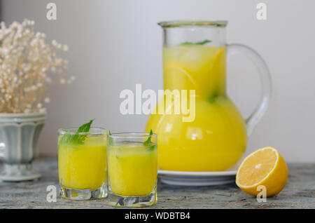 A carafe and two glasses of lemonade,  ice, mint and lemon on rustic background. Stock Photo