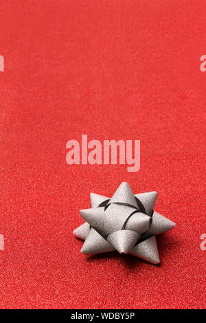 Silver gift bow on glitter red bachground with copy space. Stock Photo