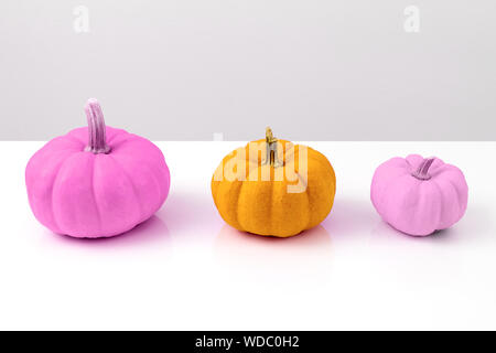 Three colored pumpkins stand in a row. Halloween interior decoration in modern kitsch style. Stock Photo
