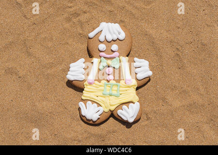 Smiling gingerbread cookie men on sandy beach, closeup flat lay. Merry Christmas and Happy New Year at beach concept Stock Photo