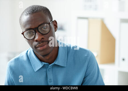 Portrait of young handsome African man in eyeglasses and in blue shirt looking at camera Stock Photo