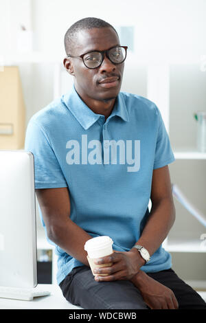 Portrait of young African man in casual clothing drinking coffee and resting after work day at office Stock Photo
