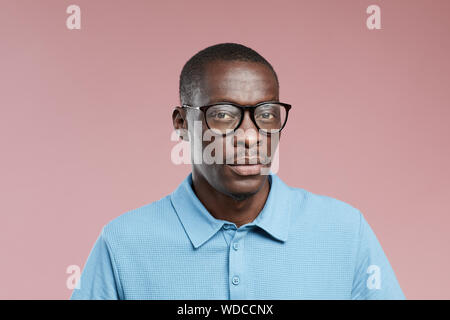 Portrait of African young man wearing eyeglasses and blue shirt looking at camera over pink background Stock Photo