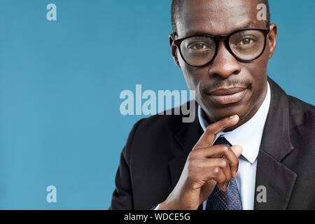 Portrait of pensive African businessman in suit and in eyeglasses thinking over new business ideas over blue background Stock Photo