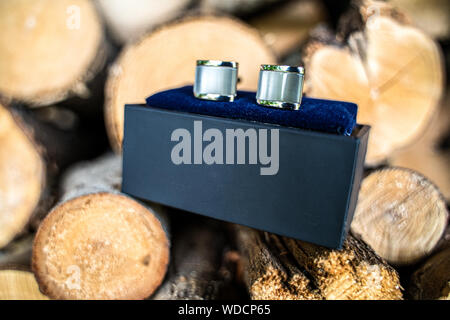 Silver cufflinks in a luxurious black box with velvet blue trim and natural background of firewood Stock Photo