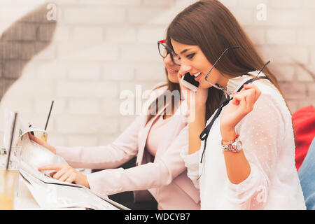 Two beautiful young women talking and cooperate in preparing for new projekt together. Beautiful woman showing information while her companion speaks Stock Photo