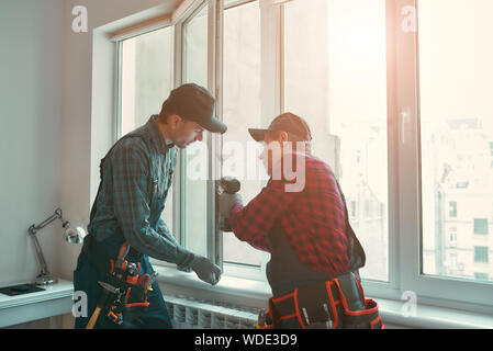 Portrait of mature men wearing uniform standing indoors and installing new windows in the apartment. Horizontal shot Stock Photo