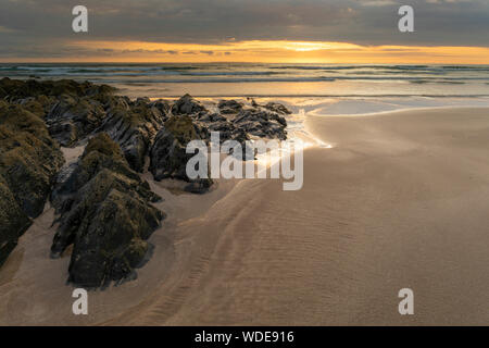 Waves surround the rocks at Combesgate beach in north devon at sunset.