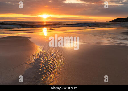 Surfers enjoy the waves at combesgate beach on north devon at sunset. Stock Photo