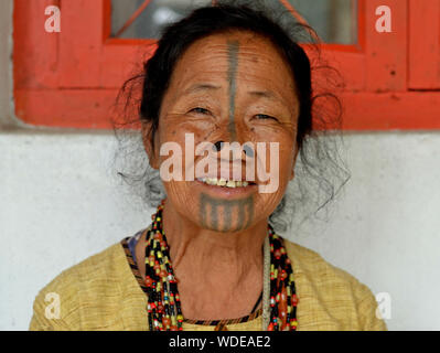 Elderly Apatani woman with black wooden nose plugs (yaeping hullo) and distinctive tribal face tattoo smiles for the camera. Stock Photo
