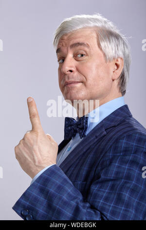 Studio portrait of senior man with a serious face expression on gray background. Mature man in suit and blue shirt with bow tie. Looking at the camera Stock Photo