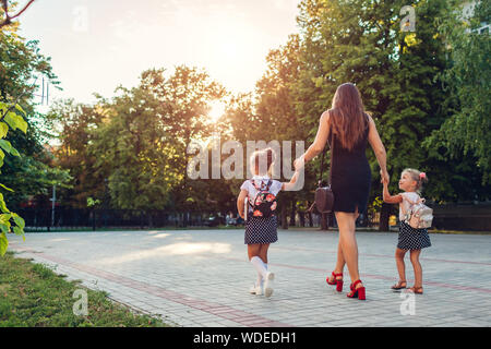 Happy mother meeting her kids daughters after classes outdoors primary school. Family goes home. Back to school concept Stock Photo