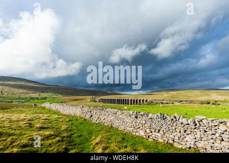 Ribblehead viaduct on a stormy day with a straight drystone wall in the foreground. Stock Photo