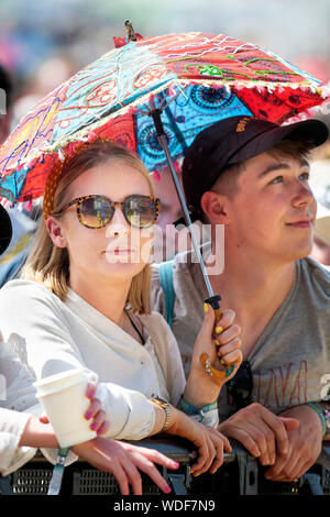 A young couple under a parasol at the Other Stage at the Glastonbury Festival 2019 in Pilton, Somerset Stock Photo