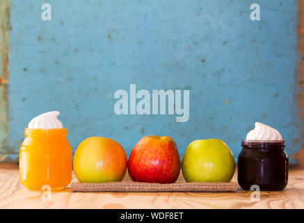 Three colored apples on a linen napkin between the glass jars with honey and blueberry jam on a background of an old blue wall. Free space for text. C Stock Photo