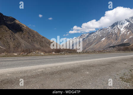 Georgia, Military Road in spring with mountain, glacier and a small village in sight, blue sky Stock Photo