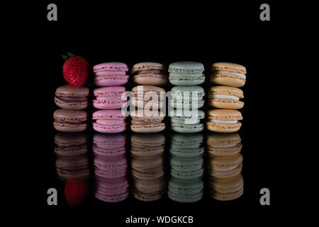 Detail of delicious brown, pink, green and yellow Macaroons stacked on a black background with a red strawberry on top Stock Photo