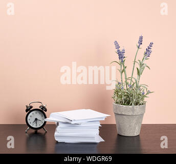 stack of white square note papers, a ceramic pot of lavender and an alarm clock on a black office desk, Scandinavian style Stock Photo