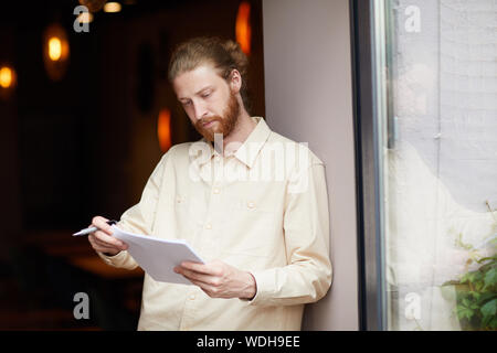 Young bearded man holding documents reading and checking it while standing outdoors Stock Photo