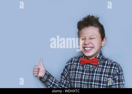 Young boy giving thumbs up portrait on violet background. Child enjoying, approving of something. Happy kid in red bowtie and checkered shirt giving l Stock Photo