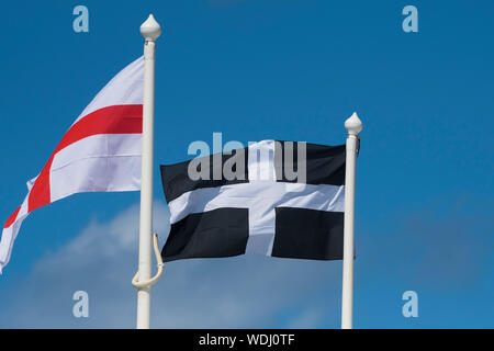 The St George’s Flag and St Piran flag flying from flagpoles against a blue sky. Stock Photo