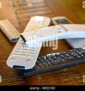 Various remote controls lying on a wooden table on top of each other. Stock Photo