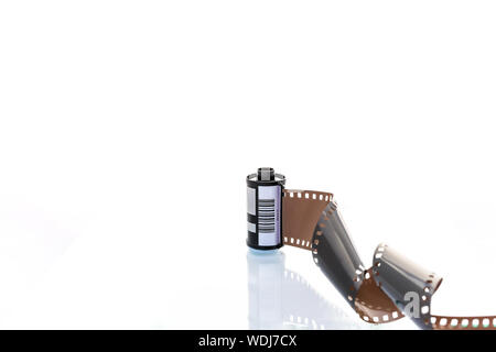 A roll of 35mm film unrolled and leading out towards the camera. Shot against a clean shite background Stock Photo
